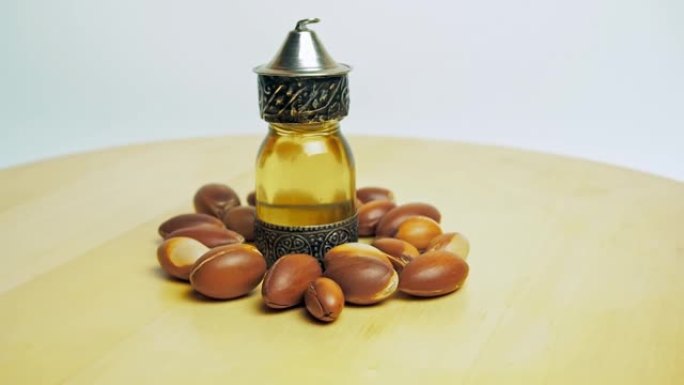 东方玻璃和金属瓶中的摩洛哥坚果油和木制桌子和白色背景上的摩洛哥坚果油运动
