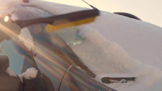 挡风玻璃上覆盖着一层厚厚的雪，用汽车刷刷下了雪。一名妇女在开车前从冰冻的汽车上清理冰雪。北欧国家的汽