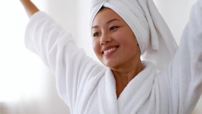 年轻宁静的亚洲女士舒展身体，在浴室洗完澡后享受健康，穿着浴袍