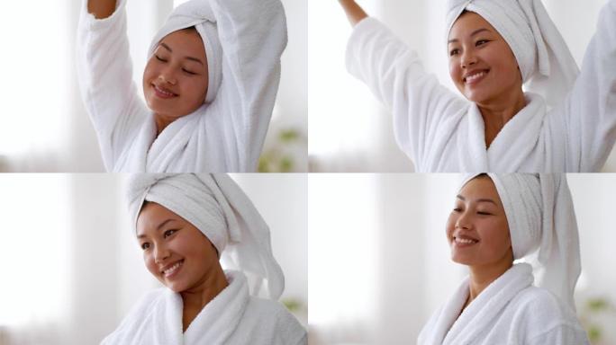 年轻宁静的亚洲女士舒展身体，在浴室洗完澡后享受健康，穿着浴袍