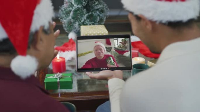 带有圣诞老人帽子的混血儿父子使用平板电脑进行圣诞节视频通话，屏幕上有男人