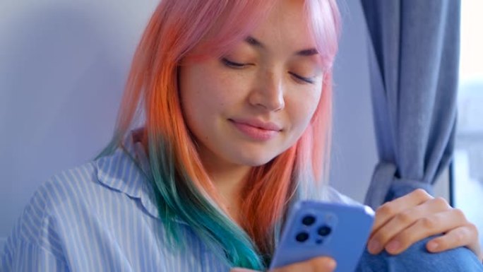 手机上有染头发的女孩浏览社交媒体新闻提要的视频。可爱的年轻女子，有色粉色头发，用现代智能手机上网