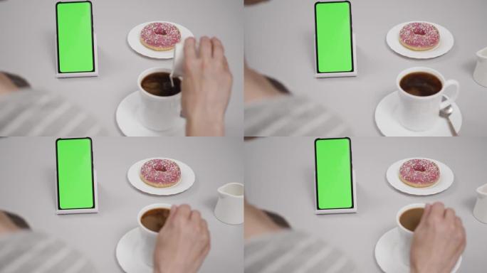 女人坐在餐桌上的咖啡甜甜圈使用带有色度键绿屏的智能手机，滚动浏览社交网络媒体在线商店互联网。智能手机