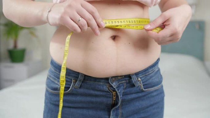腹部肥胖的年轻女子测量腰围的特写镜头。
