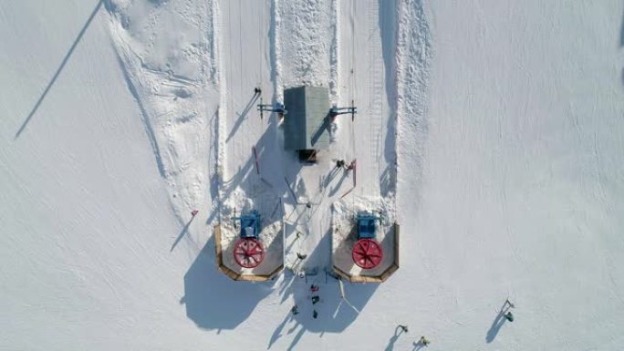 滑雪升降机底部站的空中俯视图。升降机轮在旋转，滑雪者乘滑雪缆车上升。