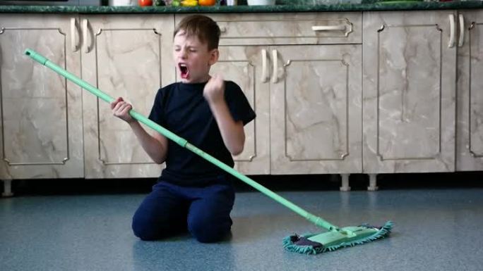 愉快地清洁。快乐的高加索男孩7-9岁洗房子的地板，哼着歌，像吉他一样用拖把。开朗的孩子喜欢做家务