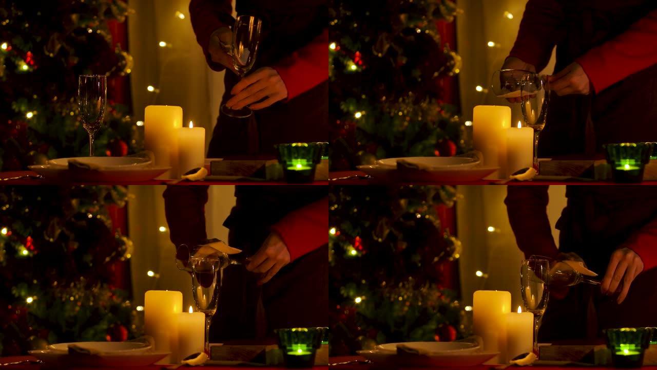 女人站在节日餐桌旁时擦拭香槟杯，摆放着燃烧的蜡烛和餐具。房间装饰是为了庆祝圣诞节或新年。双手合拢。慢