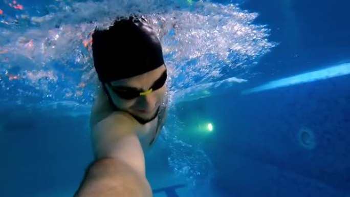 戴防水眼镜的年轻人手里拿着相机在水下游泳