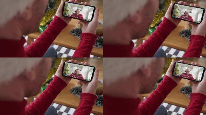 戴着圣诞老人帽子的白人男子使用智能手机进行圣诞节视频通话，屏幕上有微笑的女人