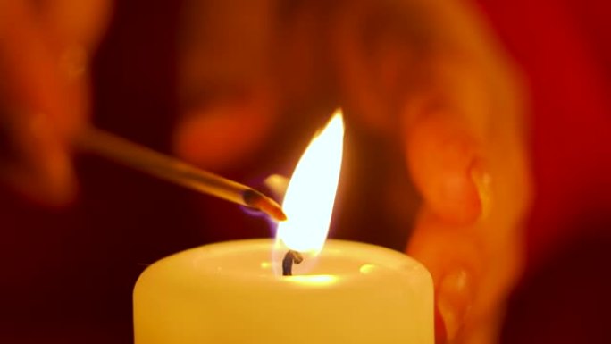 女人的手在节日桌子上点燃蜡烛。准备庆祝圣诞节或新年。模糊的红色背景。光线不足。关闭内部细节。慢动作