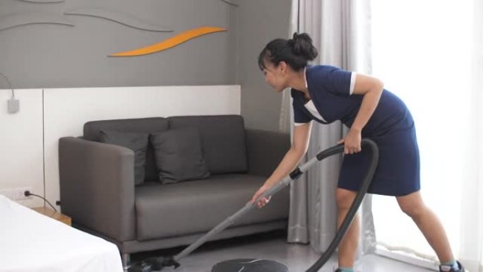 年轻女子用真空吸尘器打扫房间，客房服务