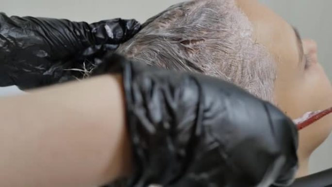戴着黑色手套的理发师的手在一个少女的头发上刷漆