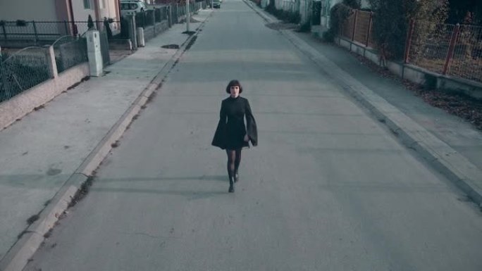 一名身穿黑衣的年轻女子走在城市街道上，慢动作无人机拍摄