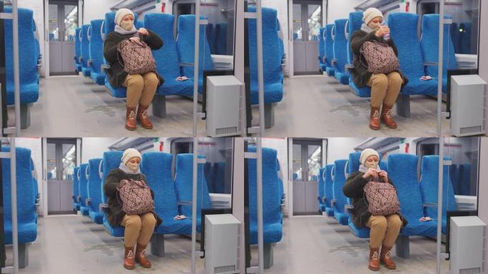 戴着面部保护面具的成熟女人正在乘坐旅客列车。她正在喝瓶装水。