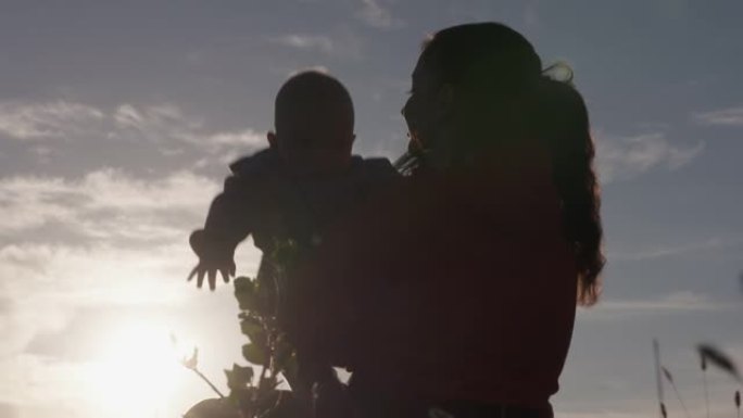 快乐母亲的剪影与他的儿子在夕阳下玩耍，妈妈与婴儿在背光中闪闪发光。