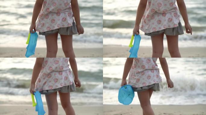 选择聚焦小女孩的背部在海滩上携带蓝色船玩具