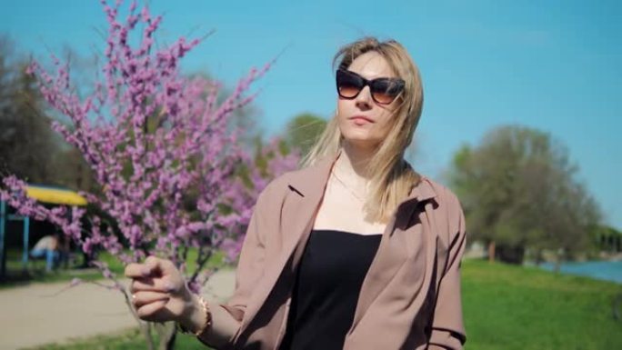 美丽的女人穿过公园，欣赏春天粉红色樱花的景色