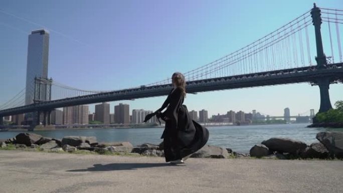 一位身穿黑色长裙的年轻女子走在美国纽约曼哈顿桥附近