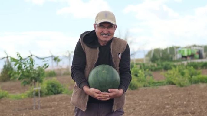 一个快乐微笑的农民在农田里的肖像，手里拿着成熟的西瓜