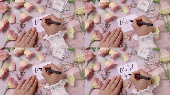 双手在粉红色的花朵附近的卡片上写下谢谢