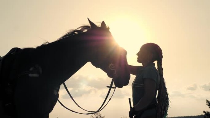 骑马。马之爱。日落时，一个年轻女子和她的马在天空背景和太阳光线背光上的轮廓。人与马之间的友谊。赤道