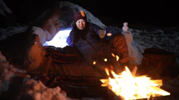 一个女人躺在冰屋旁，在雪地里的营火旁放松