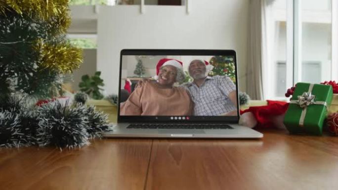 微笑的非洲裔美国夫妇戴着圣诞老人的帽子在笔记本电脑上的圣诞节视频通话中