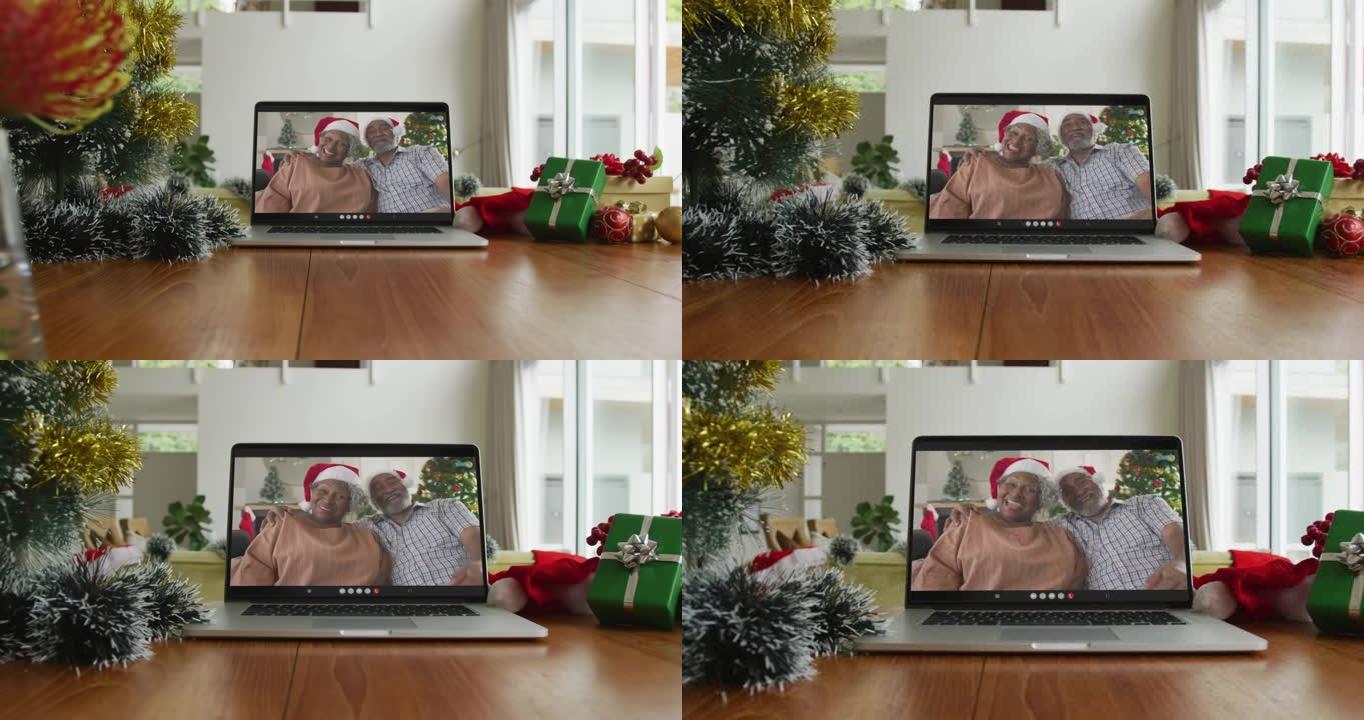 微笑的非洲裔美国夫妇戴着圣诞老人的帽子在笔记本电脑上的圣诞节视频通话中