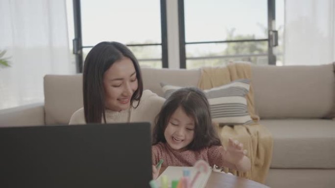 亚洲妈妈帮助学龄前女儿女孩在家使用笔记本电脑电子学习，缩放在线虚拟课程，在家上学，新常态概念