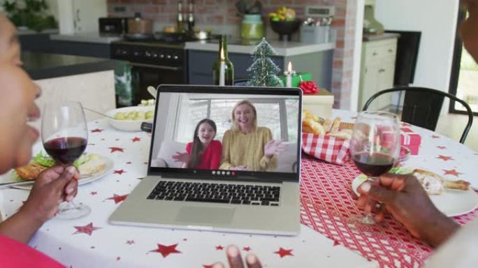 非裔美国人夫妇与葡萄酒使用笔记本电脑进行圣诞节视频通话，屏幕上有幸福的家庭