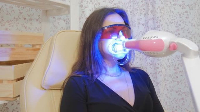 发光二极管牙齿美白。牙医椅子上的女人的肖像。牙釉质美白用紫外线灯。美丽的微笑。牙齿的健康。4K