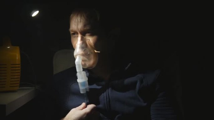 一个中年男人做喷雾器呼吸的肖像。吸入肺部有强烈的咳嗽。夜晚，灯发出的光。一个男人的脸特写