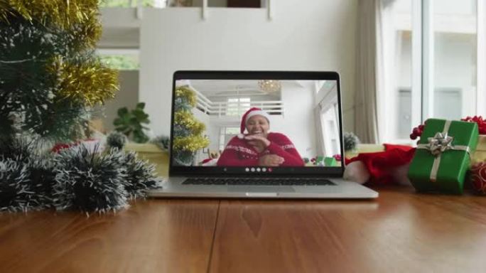 微笑的非洲裔美国妇女戴着圣诞老人的帽子在笔记本电脑上的圣诞节视频通话
