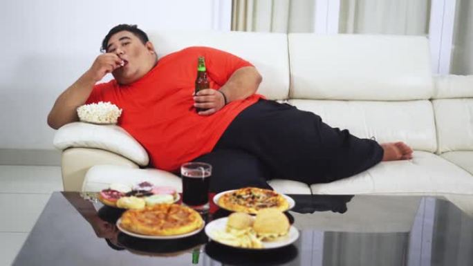 肥胖男子在餐桌上喝啤酒和垃圾食品