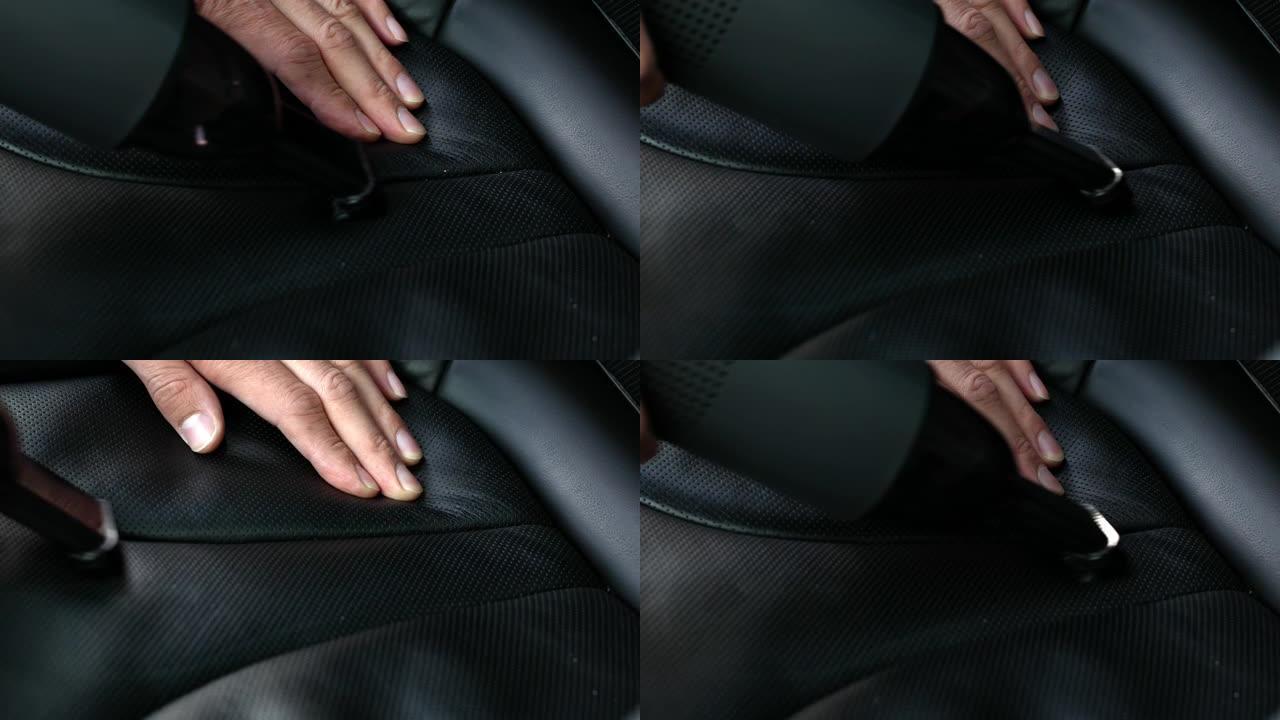 一名男子用紧凑型真空吸尘器从黑色穿孔皮革汽车座椅的接缝上清除碎屑