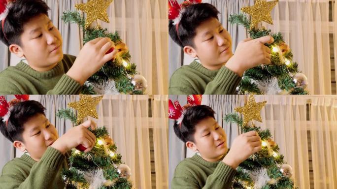 快乐的亚洲男孩戴着驯鹿发带，晚上在家装饰圣诞树，节日庆祝概念。