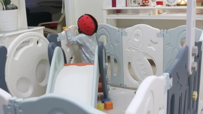 可爱的婴儿安全帽幼儿玩滑梯游戏。婴儿和幼儿安全活动中心游戏场，使儿童远离伤害。