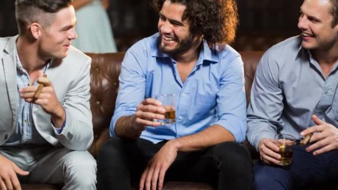 快乐的男性朋友在酒吧里聊天和抽雪茄，拿着饮料