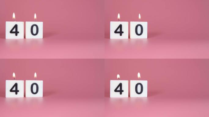 一支方形蜡烛，上面写着40号在庆祝生日或周年纪念日的粉红色背景上被点燃和吹灭。