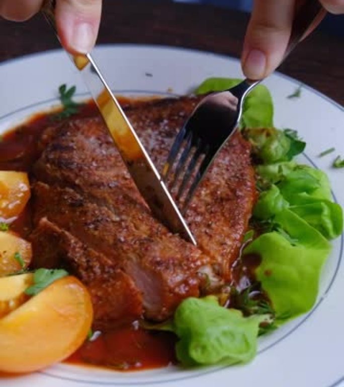 坐在桌子旁的人的手正在切一块猪排