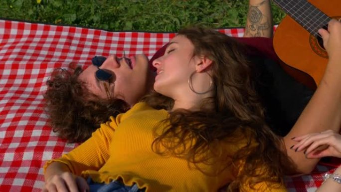 年轻的无忧无虑的夫妇躺在公园的草坪上唱歌和弹吉他