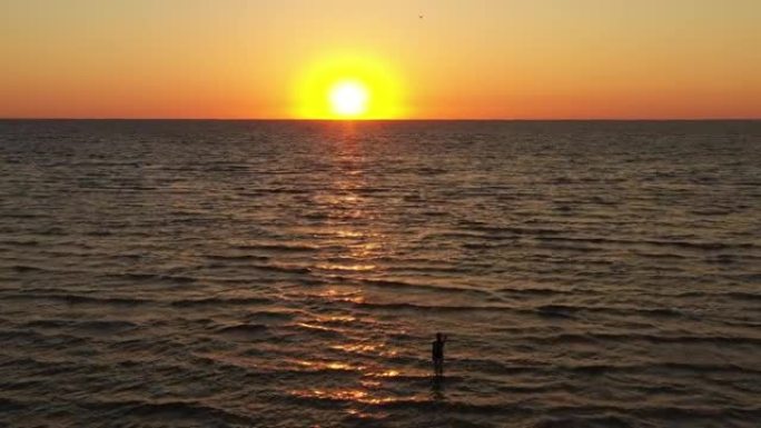 鸟瞰图无人机在海面上空飞行，日落或日出在海水上的橙色反射。年轻女子早上狼吞虎咽。放松。自然和暑假概念