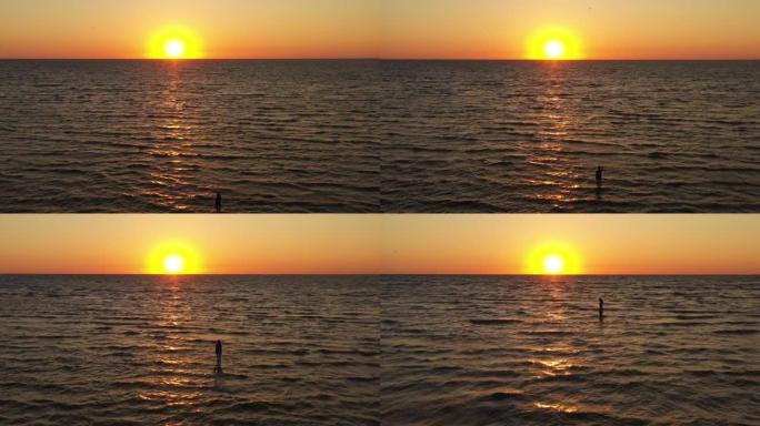 鸟瞰图无人机在海面上空飞行，日落或日出在海水上的橙色反射。年轻女子早上狼吞虎咽。放松。自然和暑假概念