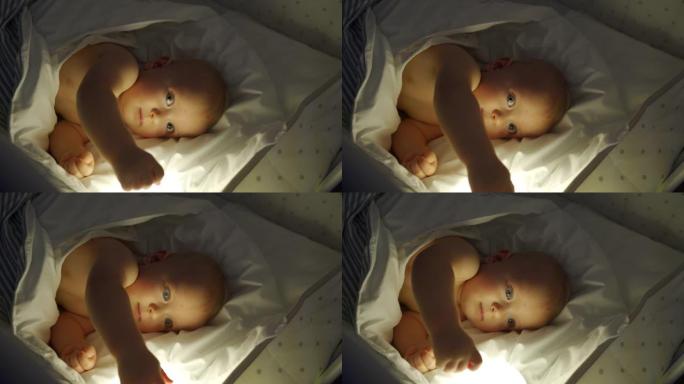 晚上，在夜灯的灯光下，将9个月的男婴包裹在婴儿床中。快乐婴儿从襁褓中挣脱出来的脸。