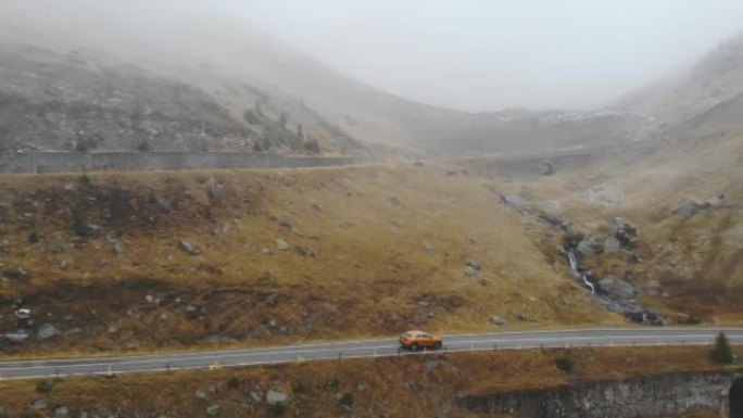 橙色汽车在秋天穿越雾山公路。秋季乡村路线自动驾驶的航拍。SUV通过风景优美的方式行驶。旅程的概念。顶