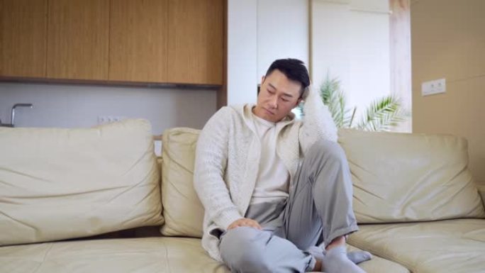 无聊的朋友年轻的亚洲男人独自坐在家里的沙发上。想念坐在公寓沙发上的男性。
