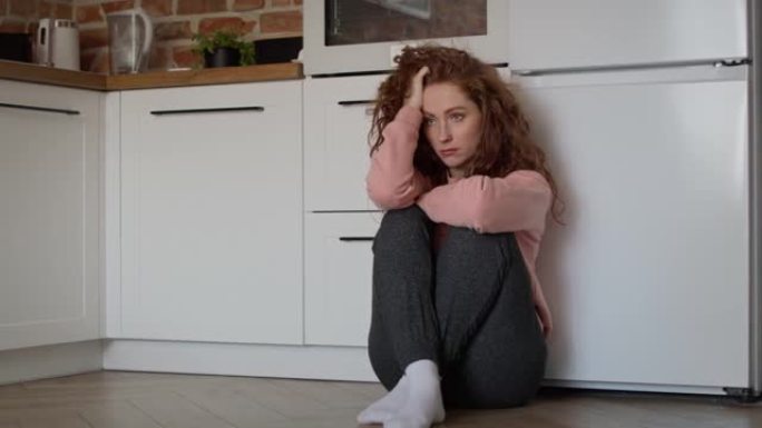 悲伤的年轻白人妇女悲伤地坐在厨房的地板上。用8k的红氦相机拍摄。