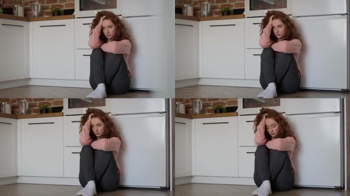 悲伤的年轻白人妇女悲伤地坐在厨房的地板上。用8k的红氦相机拍摄。