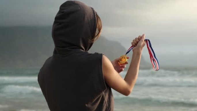 海洋附近海滩上的体育女孩胜利地举起了冠军勋章