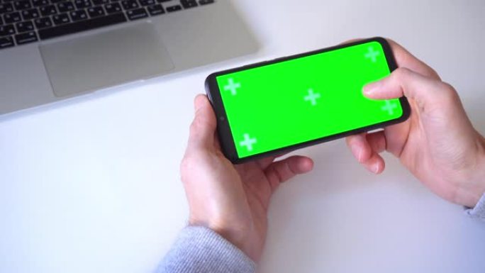 特写。4k。一名男子双手握着智能手机，按下手指，滚动绿色屏幕的色度键。点击应用程序图标，玩游戏，用手